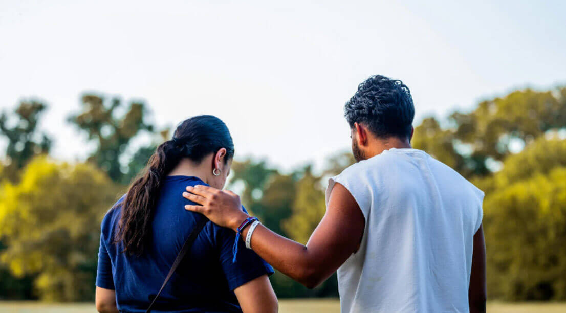 One person places a supportive hand on another’s shoulder while walking outdoors, symbolizing encouragement and connection in recovery.