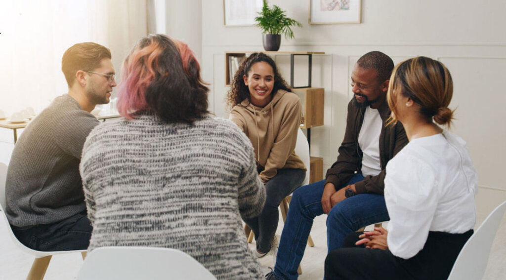 A small group of people sitting in a circle during a supportive group therapy session, talking and listening.