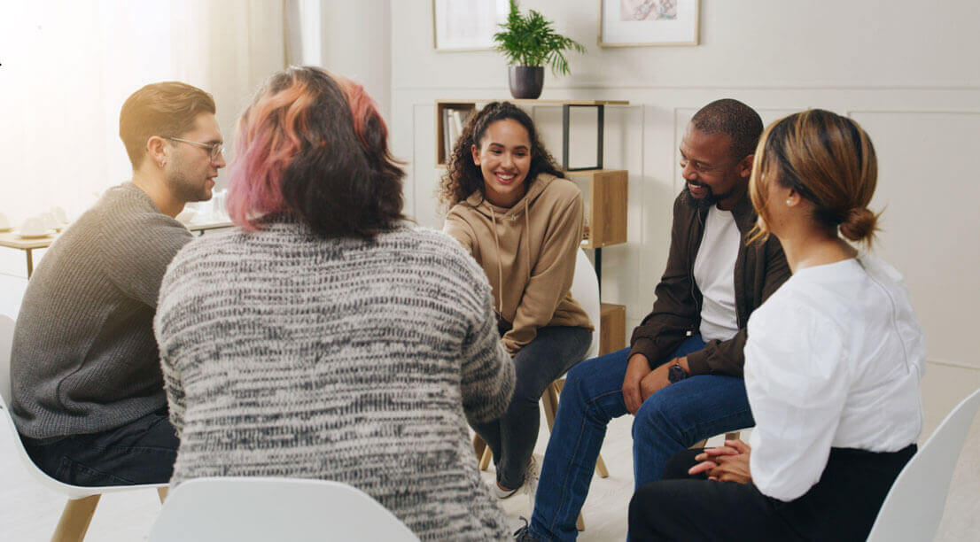 A small group of people sitting in a circle during a supportive group therapy session, talking and listening.