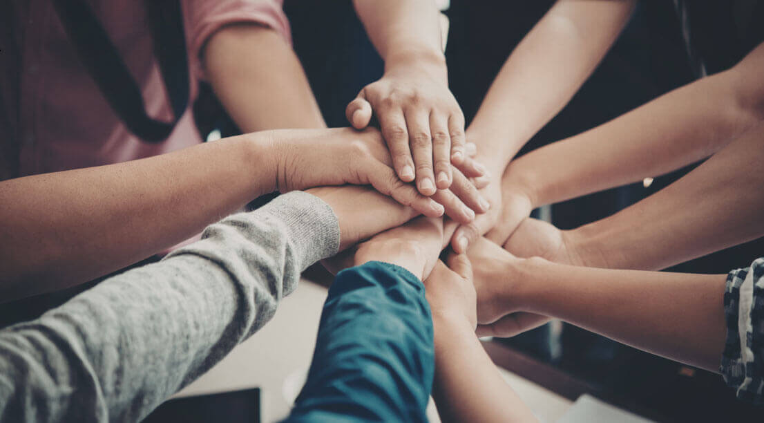 A group of people placing their hands together in a circle, symbolizing teamwork and support in recovery.