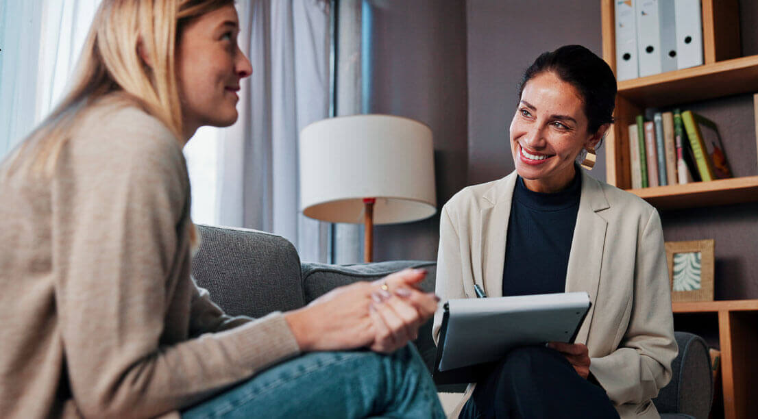 A therapist smiling and taking notes while speaking with a client during a counseling session.