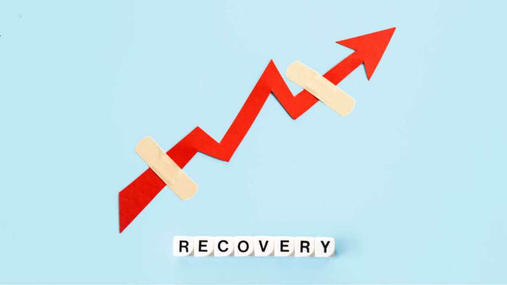 A red paper arrow trending upward with two bandages covering breaks in its path, paired with letter tiles spelling 'RECOVERY' on a light blue background.