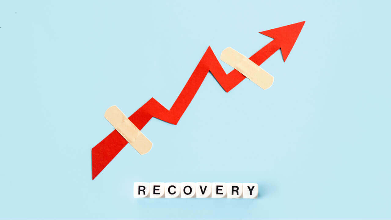 A red paper arrow trending upward with two bandages covering breaks in its path, paired with letter tiles spelling 'RECOVERY' on a light blue background.
