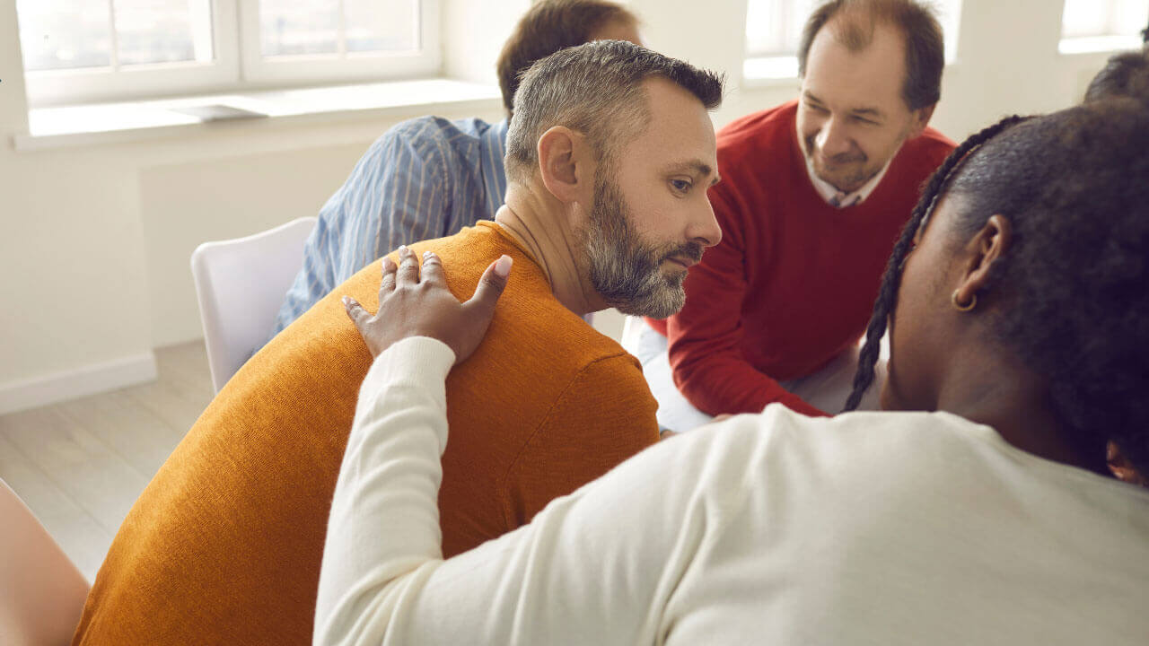 A group member offers a reassuring hand to a man during a recovery support meeting.