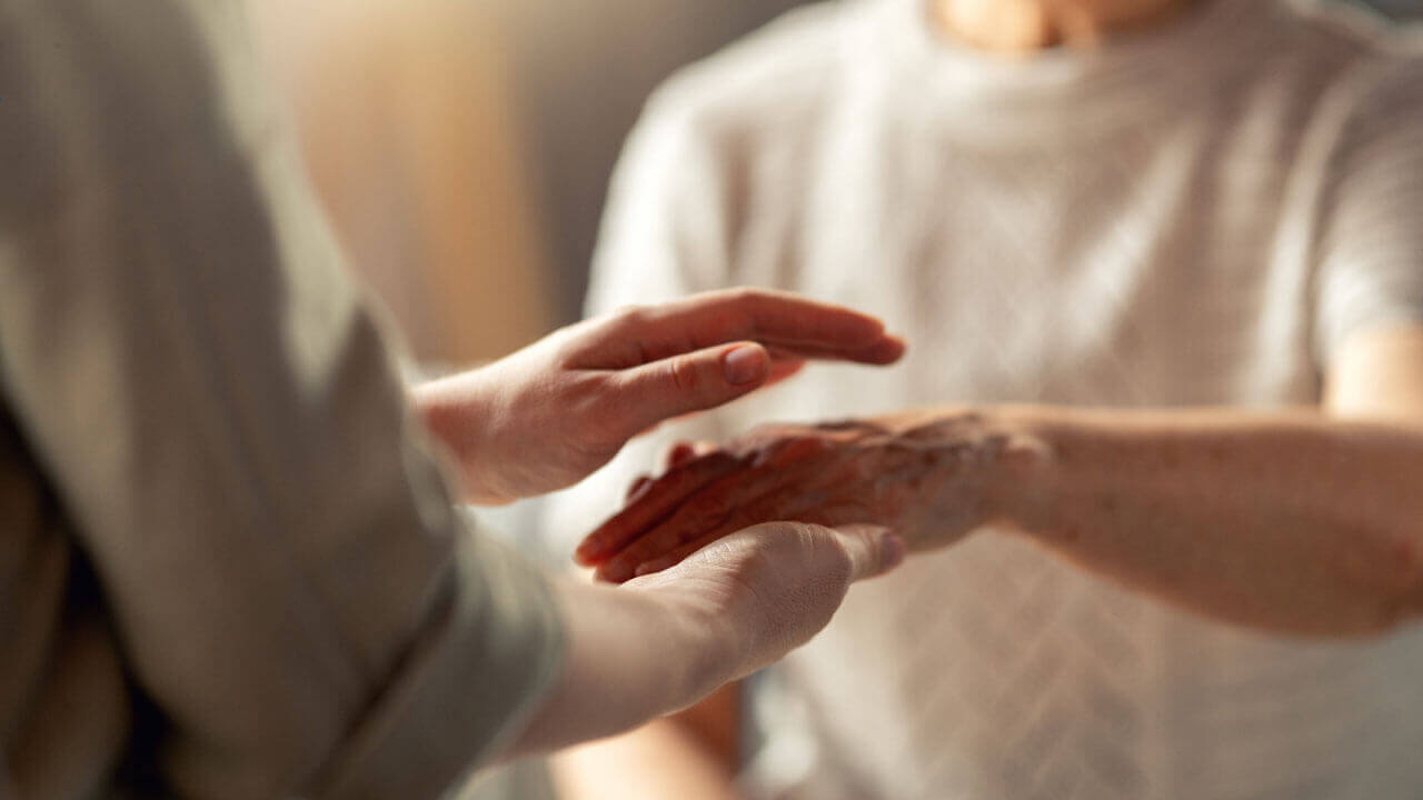 One person gently holds another person’s hands in a gesture of care and support.