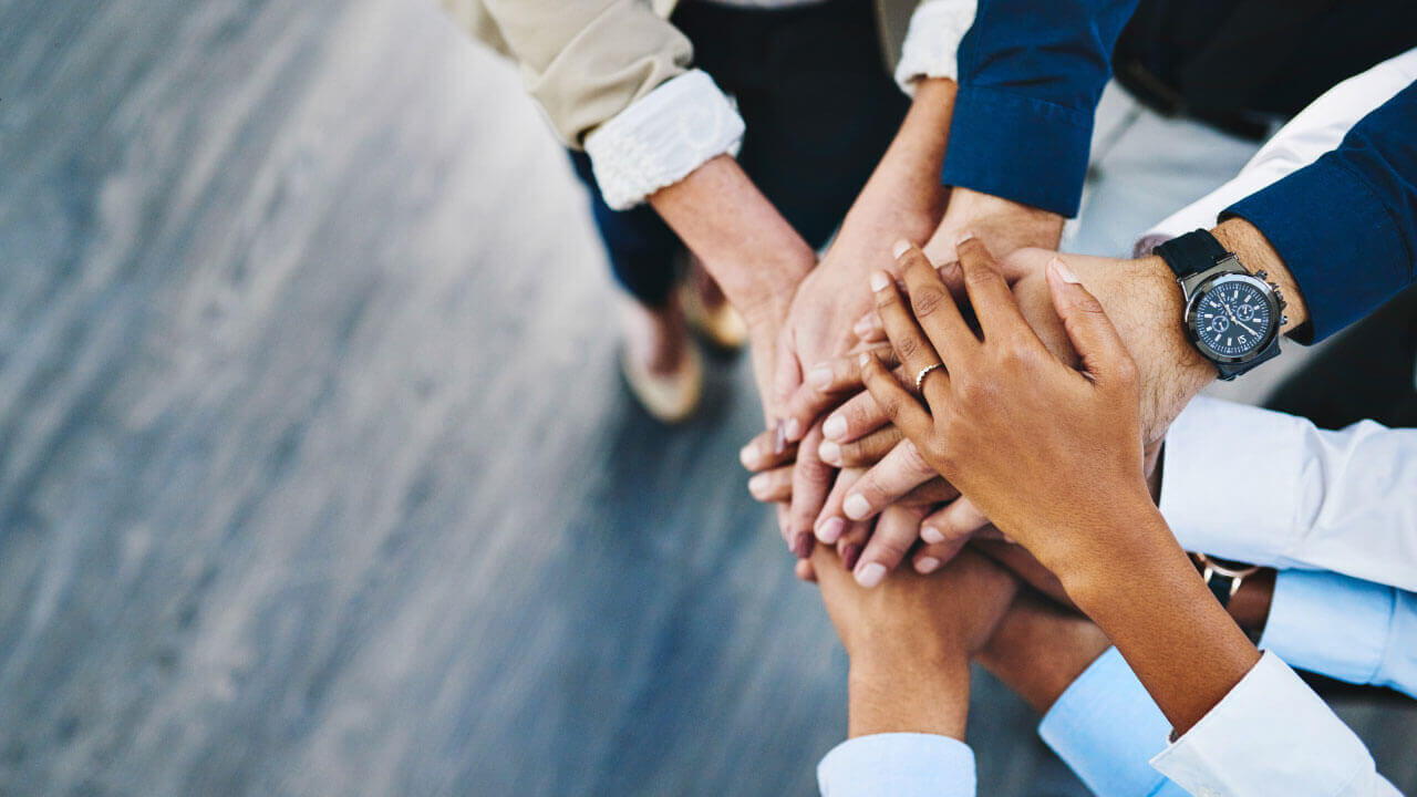 A diverse group stacks their hands together to symbolize unity and mutual support.