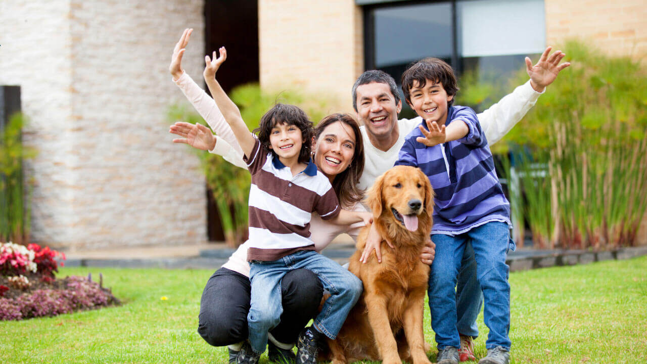 Cheerful family of four with raised arms posing outdoors with a golden retriever.