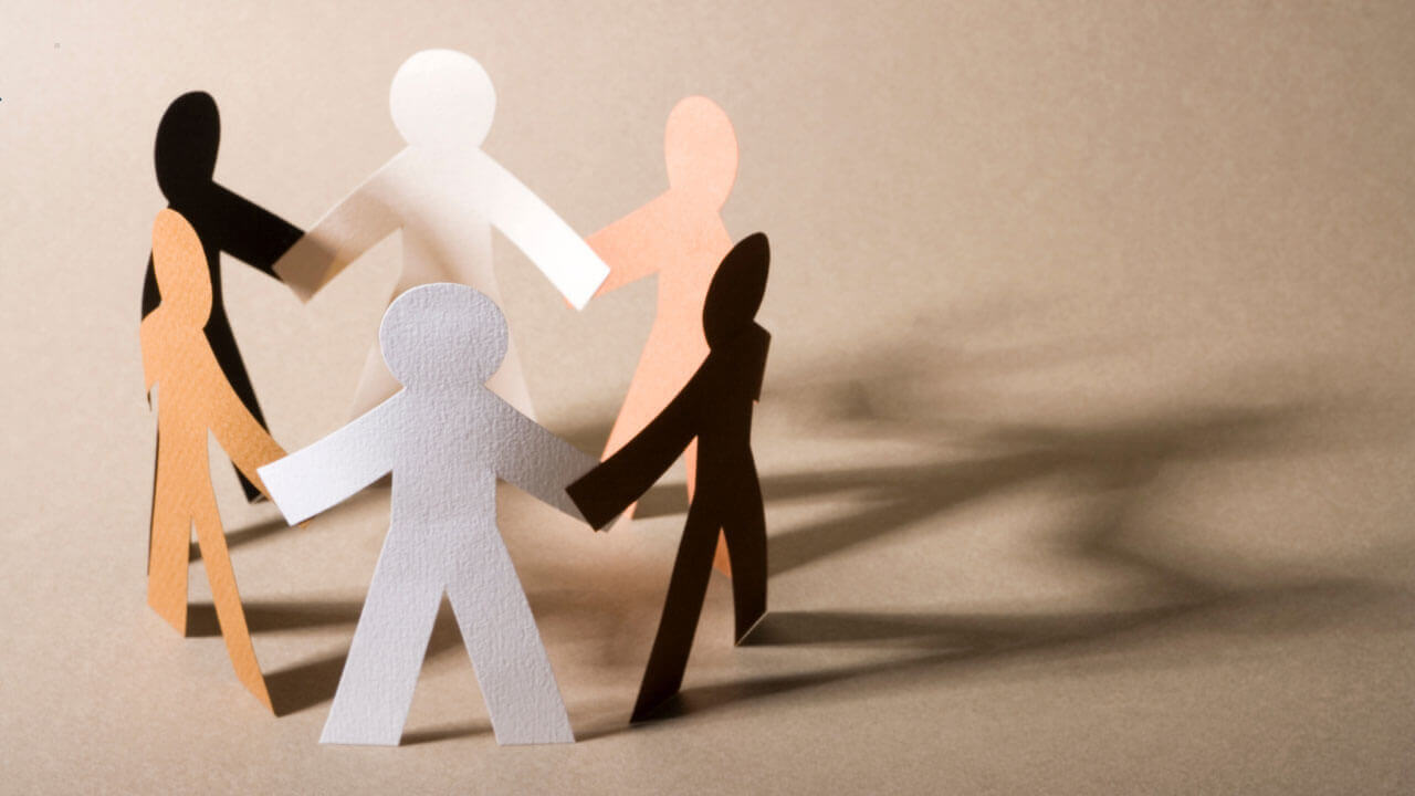 A circle of paper cutout figures in varied skin tones holds hands on a tan background.