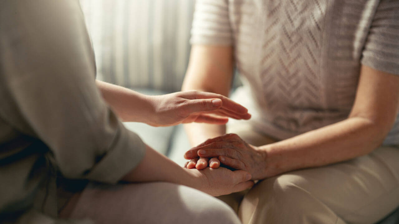 Close up of two people holding hands together in a gentle comforting gesture.