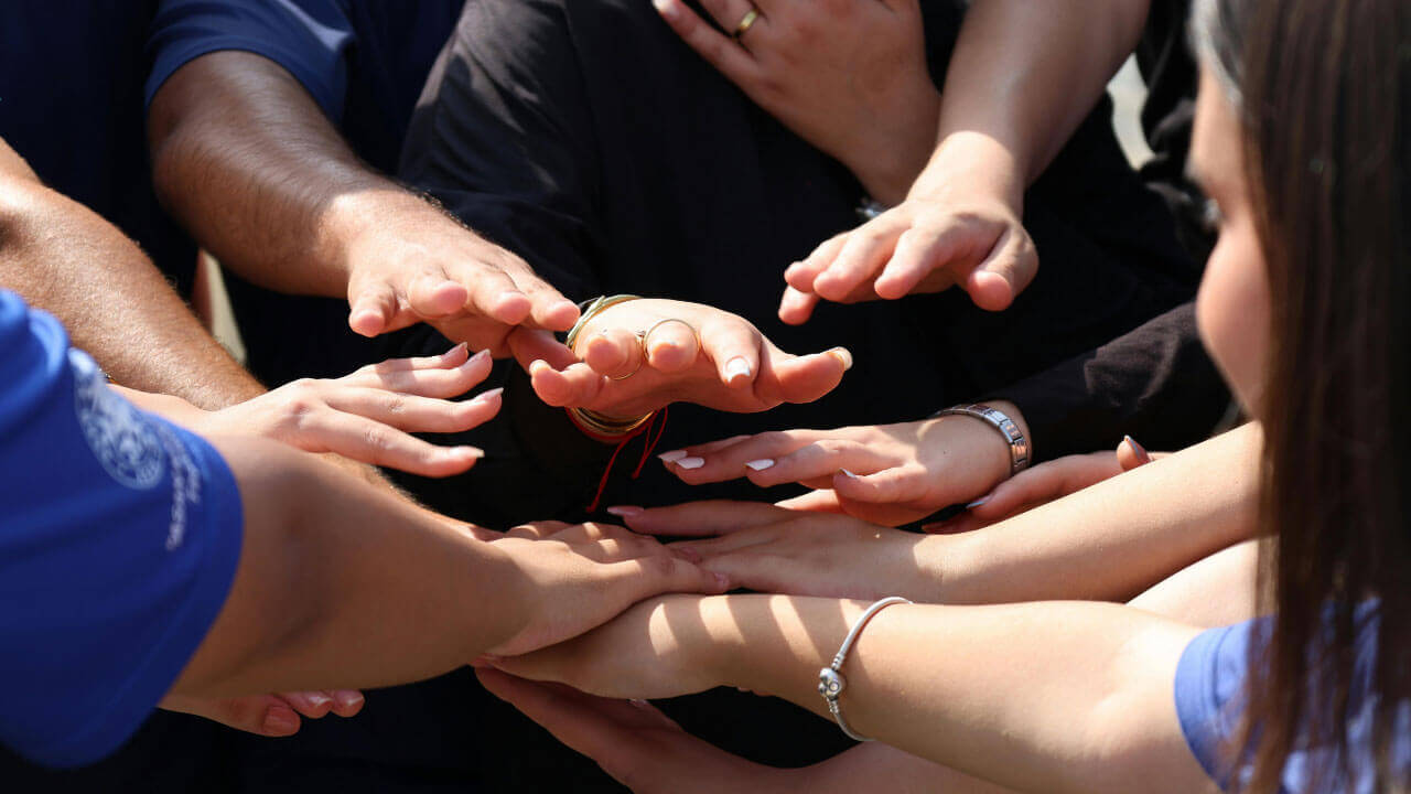 A close-up of many hands reaching toward the center in a gesture of group unity.
